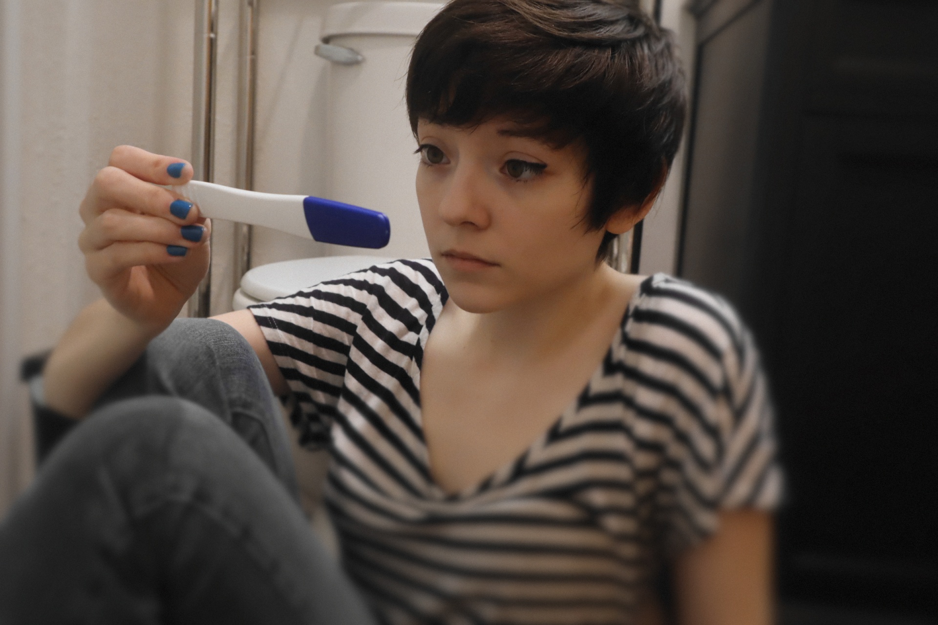 A young woman in a striped shirt looking at a pregnancy test